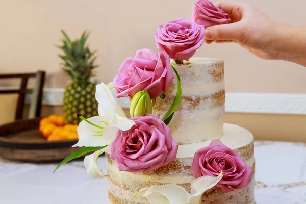 Woman decorating naked cake with flowers. — Stock Photo, Image