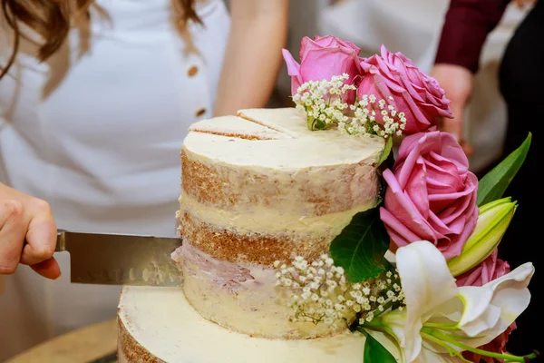 Noiva e noivo em vestido branco corte camada bolo de casamento nu, decorado com flores frescas . — Fotografia de Stock