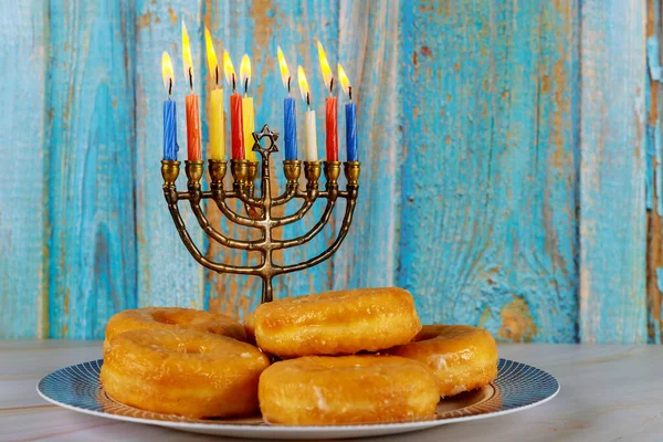 Jewish holiday Hanukkah. Donuts and menorah with burning candles on plate.