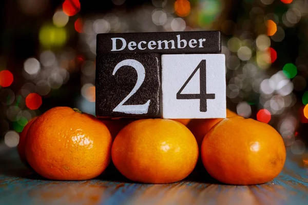 Kerstavond, 24 december houten kubus kalender met mandarijnen op kerstboom verlichting achtergrond. — Stockfoto