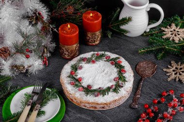 Siyah masa üzerinde kranberiye süslemeli bayram pastası ve yanan mumlar..