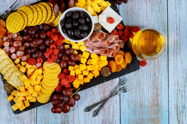 Tabla de embutidos con queso, aceitunas, frutas, jamón y vino sobre mesa de madera . — Foto de Stock