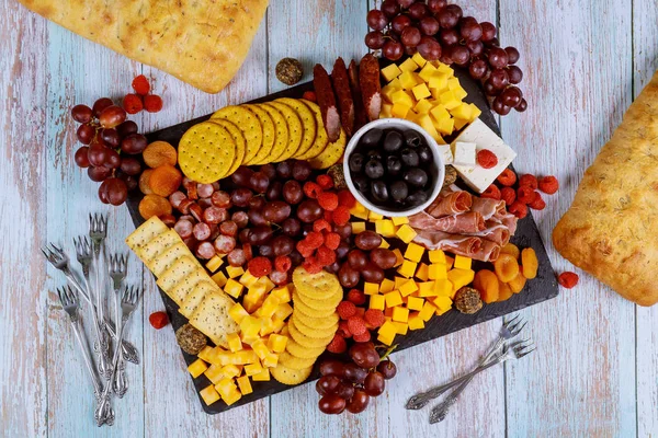 Surtido de charcutería, queso, aceitunas, frutas y jamón sobre mesa de madera . — Foto de Stock