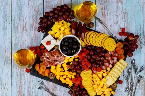 Tabla de embutidos con queso, aceitunas, frutas, jamón y vino sobre fondo de madera . — Foto de Stock