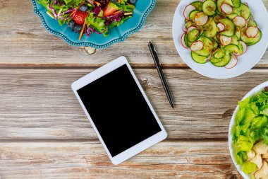 Tablet ve ahşap masada çeşitli salatalar..
