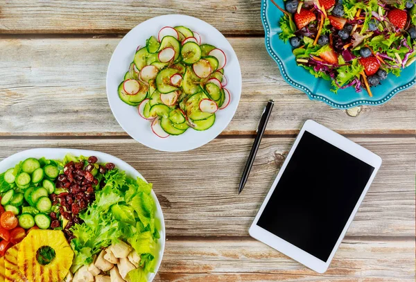 Various salads with tablet and pen on wooden table. — Stock Photo, Image