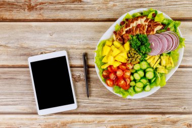 Tablet ve kalemle ahşap masada salatalar..