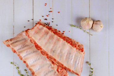 Uncooked pork ribs with garlic and herbs on white background.