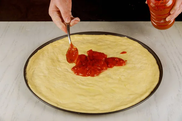 Chef pouring pizza marinara on raw dough. — Stock Photo, Image