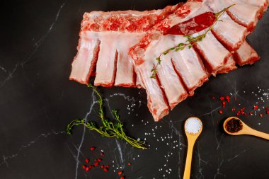 Raw fesh spare ribs with seasoning on black background.