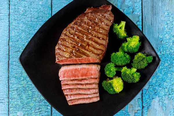 Medium rare beef sirloin with broccoli on black plate.