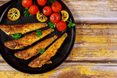Lezzetli kızarmış balık, limonlu ve domatesli siyah tavada servis ediliyor..