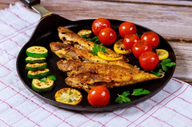 Lezzetli kızarmış balık, ahşap masada siyah tavada sebzelerle servis edilir..