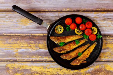 Ahşap arka planda tavada domates ve limonla kızartılmış küçük balık. Üst görünüm.