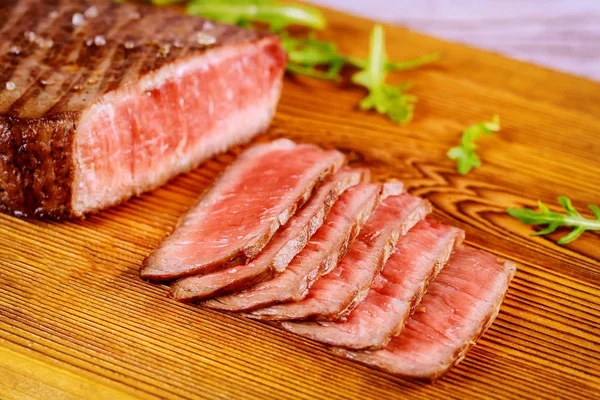 Grilled sliced rare angus beef steak on wooden board. Close up.