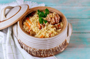 Sebzeli Özbek pilavı ve ahşap arka planda kapaklı tencerede et.