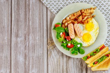 Kahvaltı için lezzetli yiyecekler. Yumurta, pastırma, salata ve ahşap masada ızgara peynirli sandviç..