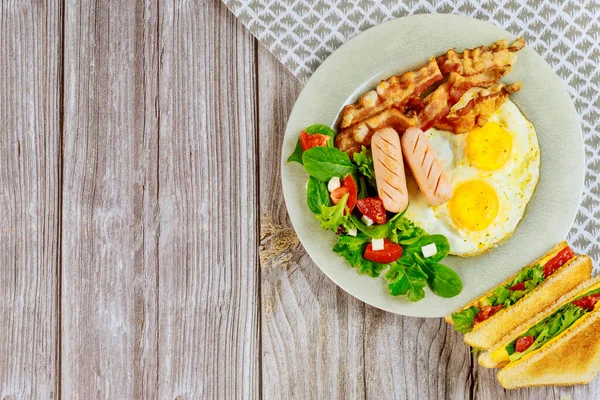 Kahvaltı için lezzetli yiyecekler. Yumurta, pastırma, salata ve ahşap masada ızgara peynirli sandviç..
