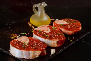 Ossobuco malzemeleri hazırlıyor. Çiğ sığır inciği kemiği ve siyah arka planda baharatlar..