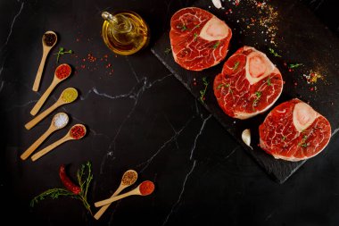 Çiğ sığır inciği kemiği ve siyah arka planda ossobuco yemeği hazırlamak için baharatlar. Üst görünüm.