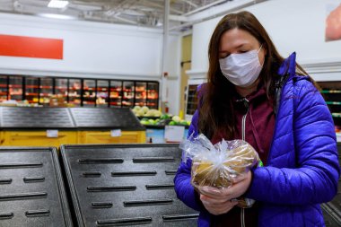 Yüz maskeli bir kadın son patates torbasını boş raflarla dükkanda tutuyor. Coronavirus konsepti.