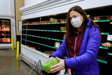 Yüz maskeli bir kadın marketten boş raflarla marul alıyor. Coronavirüs salgını konsepti.