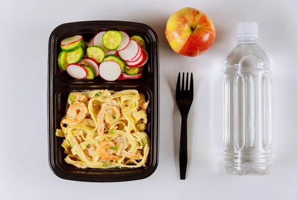 Ready meal to eat on food container with fork, water and apple.
