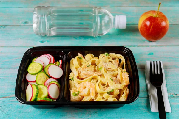 Ready meal on food container with fork, water and apple.