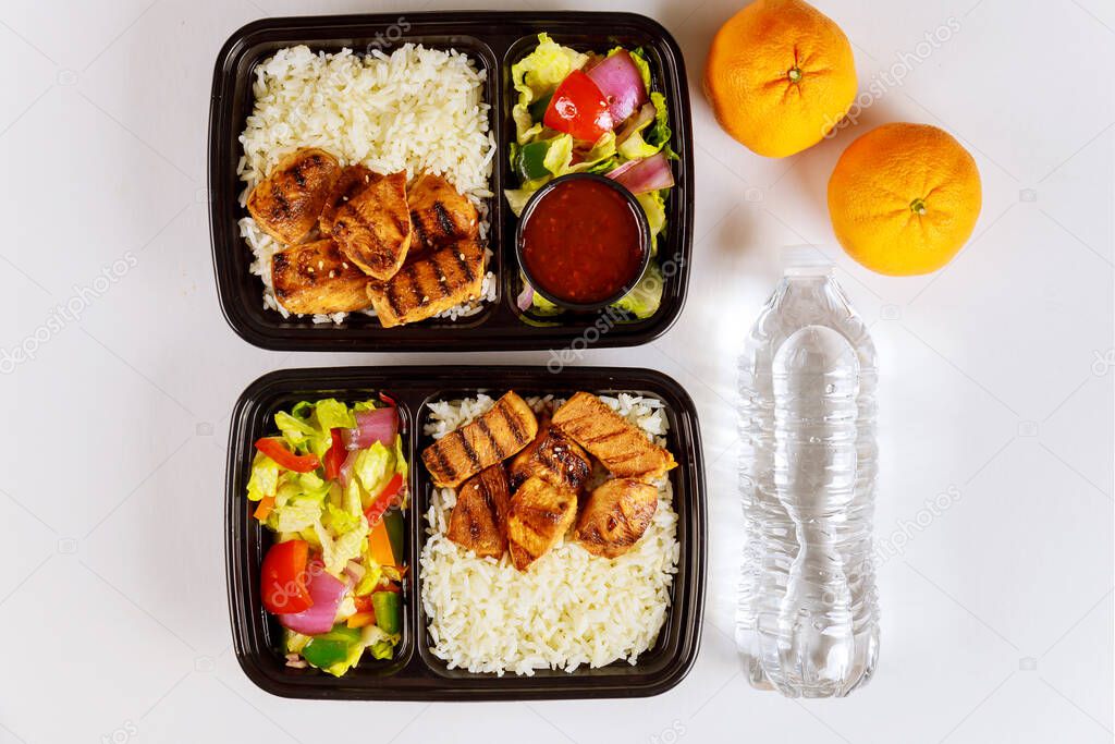 Ready meal to eat on food container with fork, drink and orange.