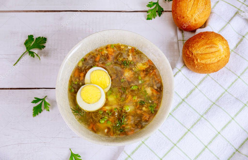 Green vegetable soup with egg and crusty rolls on wooden background.