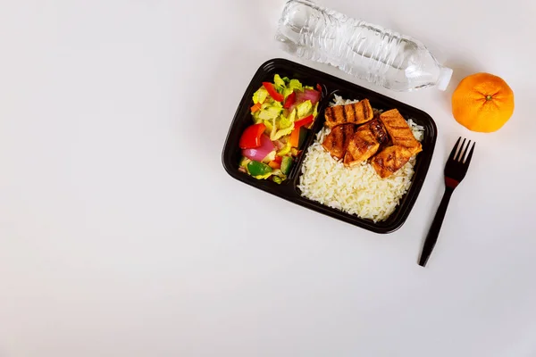 Ready meal to eat on food container with fork, drink and orange.