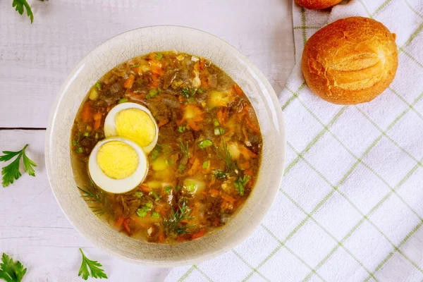 Vegetable soup with egg and crusty rolls on wooden background.