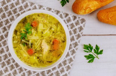 Bir kase tavuklu şehriye çorbası ve beyaz masada ekmek..