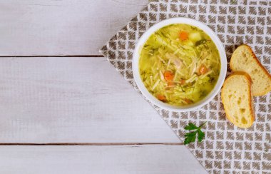 Maydanoz ve ekmekle birlikte beyaz tabakta tavuk çorbası. Üst görünüm.