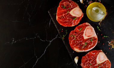 Pişmemiş çiğ biftek kemiği ve siyah tahtada ossobuco yemeği hazırlamak için baharatlar...