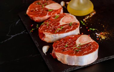 Çiğ sığır incik kemiği ve siyah tahta üzerinde ossobuco yemeği hazırlamak için baharatlar...