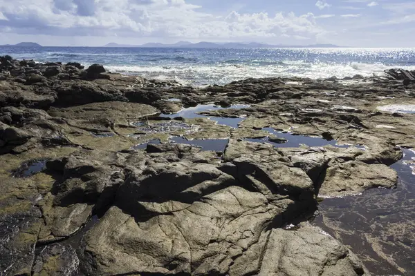 Глубоко синяя вода с волнами, белой пеной и вулканическими породами — стоковое фото
