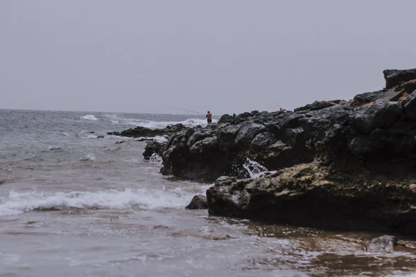 Fisherman fishing over volcanic rock in atlantic sea — Stock Photo, Image