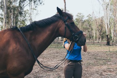 Genç bir kadın ata binmeden önce ahırda atına sarılıyor.