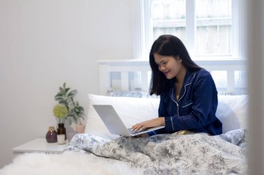 Genç Asyalı gülümseyen kadın odasında dizüstü bilgisayarla çalışıyor. Mutlu sabahlar