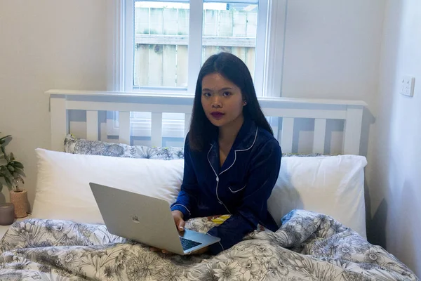 Young asian smiling woman working on laptop in her bedroom. Happy morning