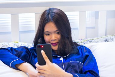 Asyalı kadın cep telefonuyla yatağa uzandı.
