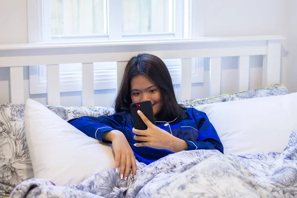 Asian woman lay down on the bed using a mobile
