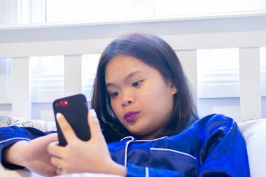 Asyalı kadın cep telefonuyla yatağa uzandı.