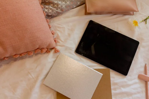 Boş tablet, iki defter, kalem kılıfı ve yatakta pembe yastık.