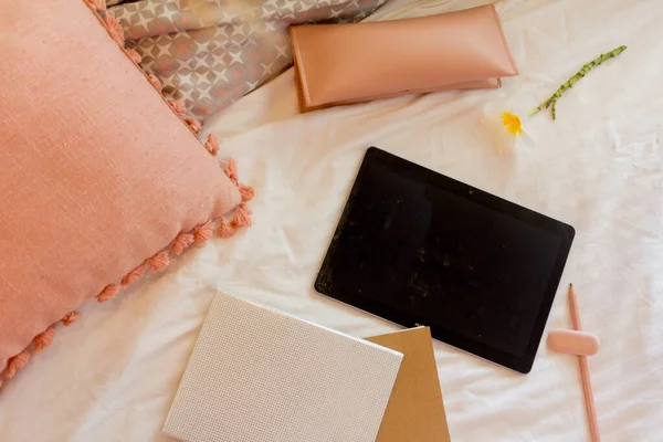Boş tablet, iki defter, kalem kılıfı ve yatakta pembe yastık.
