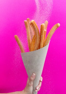 Pembe arka planda kağıt torbada şekerli Churros.