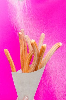 Pembe arka planda kağıt torbada şekerli Churros.
