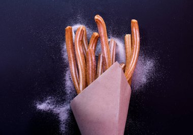 Churros taze sıcak yapışır. Koyu arkaplanda kağıt torbada şeker var.