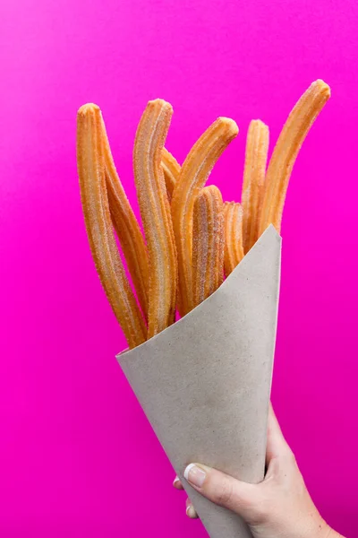 Pembe arka planda kağıt torbada şekerli Churros.